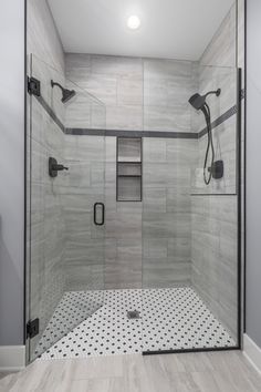 a walk in shower sitting next to a white wall and floor covered in black and white tiles