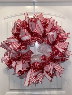 a red and white wreath hanging on the front door with ribbon around it's edges