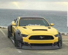 a yellow sports car parked in a parking lot next to the ocean on a cloudy day