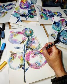 someone is painting flowers on paper with watercolors