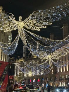 an angel statue is lit up in the night sky over a busy street with cars and pedestrians