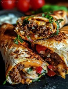 two burritos cut in half on a black plate with tomatoes and lettuce