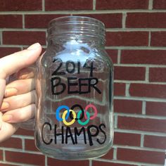 a person holding up a mason jar with the words beer and olympics painted on it