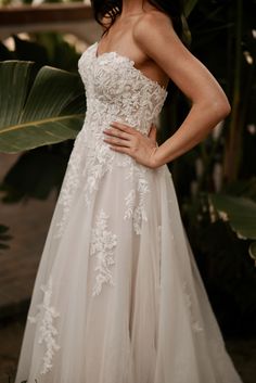 a woman in a wedding dress standing next to a palm tree with her hands on her hips