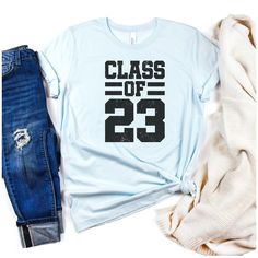 **Due to the influx of holiday shipping, please note that any orders purchased after Dec. 12th will most likely be delivered after Christmas.**Where are my senior graduates of 2023?! You need to rock this cute, lightly distressed Class Of 2023 shirt. It is the perfect gift for any senior in your life. The lightly distressed design is very trendy but it also has a classic varsity letter font. This soft cotton short sleeve tee is unisex (not fitted) and fits true to size. Soft cotton and quality p Casual Screen Print Tops For College Events, Casual Screen Print Tops For College, Graduation T-shirt With Letter Print In Relaxed Fit, Casual Graduation Shirt With Text Print, Casual Letter Print Shirt For Graduation, Casual Shirt With Text Print For Graduation, Graphic Print Tops For College Events, School Spirit Cotton Tops For Graduation, Cotton Tops For Graduation With School Spirit