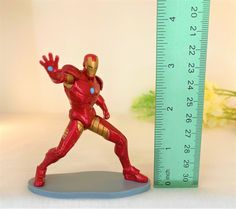 a toy iron man standing next to a ruler