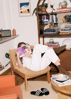 a woman sitting in a chair reading a book with her feet up on the coffee table