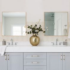 a bathroom with two sinks, mirrors and a vase filled with flowers on the counter