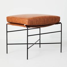 a brown leather ottoman with black metal frame and footrests on white flooring