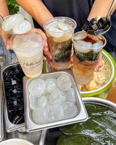 three people are holding drinks in their hands while sitting at a table full of food