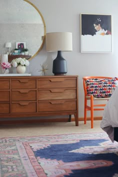 a bedroom with a dresser, mirror and lamp on it's side table in front of the bed