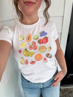 Embrace the charm of our vintage fruit collage top, a y2k inspired baby tee featuring a delightful collage of painted fruits. This isn't just any fruit graphic tee--it's a girly top perfect for adding a touch of nostalgia to your wardrobe. With its playful design and farmers market vibes, it's a nod to 90s fashion that's both fresh and timeless. Click now to add it to your cart and elevate your style! 🫧 SIZING * Available sizes: XS -XL  * This garment is true to size, but size down if you prefer a more fitted look. * Keep in mind, this garment is in youth sizing to achieve the baby tee fit, so it will be more snug around the bust. * Refer to the size chart in the photos for details, we recommend measuring a shirt you already own and love in order to get the perfect fit. 🫧 MATERIALS * 100 Y2k Style Short Sleeve T-shirt With Fruit Print, Y2k Strawberry Print Short Sleeve Tops, Y2k Short Sleeve Tops With Strawberry Print, Cute White Tops With Fruit Design, Cute White Fruit Design Tops, Y2k Fruit Print Short Sleeve Tops, Y2k Style Fruit Print Short Sleeve Tops, Y2k Short Sleeve Top With Fruit Print, Cute Cotton Tops With Fruit Design