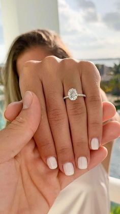 a woman holding up her engagement ring with the ocean in the backgrouund