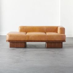 an orange leather couch sitting on top of a cement floor next to a white wall