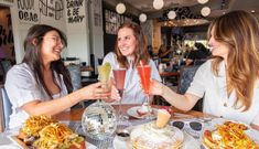 three women sitting at a table with food and drinks