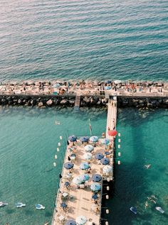 an aerial view of a pier with umbrellas and people swimming in the water next to it