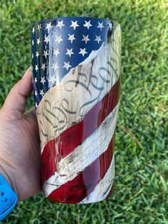 a hand holding a coffee cup with the american flag painted on it in front of green grass