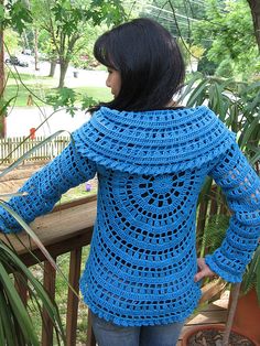 a woman wearing a blue crocheted sweater standing on a porch next to potted plants