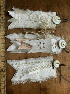 three pieces of white fabric with buttons and lace on them sitting next to a ruler