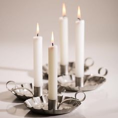 four white candles sitting on top of metal trays