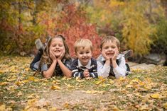 three young children laying on the ground with their hands in their pockets and smiling at the camera