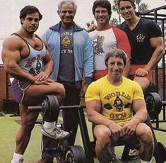 a group of men standing next to each other in front of a barbell machine