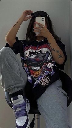 a woman taking a selfie with her cell phone while sitting on a stool in front of a wall