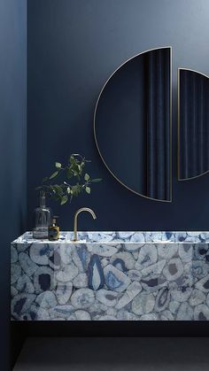 a bathroom with blue walls and a marble sink in front of a round shaped mirror