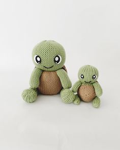 two green stuffed animals sitting next to each other on a white surface with one holding the other's hand