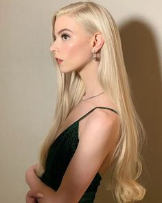 a woman with long blonde hair standing in front of a wall wearing a green dress