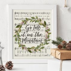 a framed print with the words go tell it on the mountain surrounded by evergreen leaves and pine cones