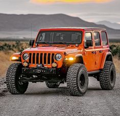 an orange jeep driving down a dirt road