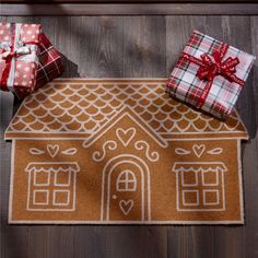 two wrapped presents sitting on top of a door mat next to a house shaped like a gingerbread house