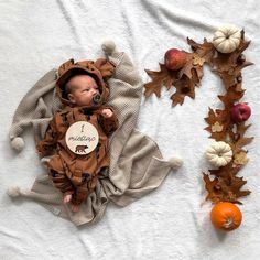 a baby laying on top of a white blanket next to pumpkins and other decorations