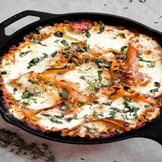 a pizza in a black pan with cheese and herbs on the top, next to a sprig of rosemary