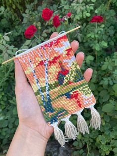 a hand holding a needle - embroidered pouch with tassels and flowers in the background