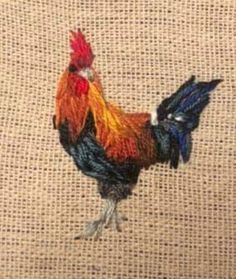 a colorful rooster standing on top of a piece of burlied fabric with red, orange and blue feathers