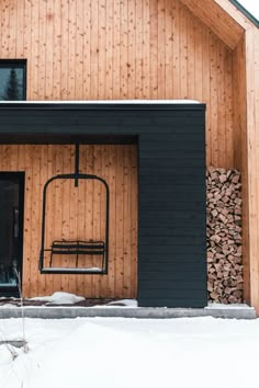 a wooden house with a metal chair on the front porch and snow covered ground around it