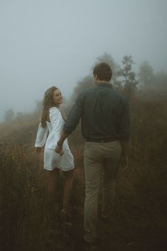 a man and woman holding hands walking through the fog