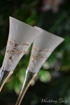 three champagne flutes with gold designs on them sitting in front of some flowers and greenery