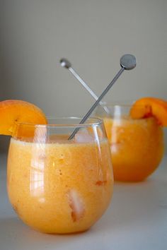 two glasses filled with orange juice and silver spoons