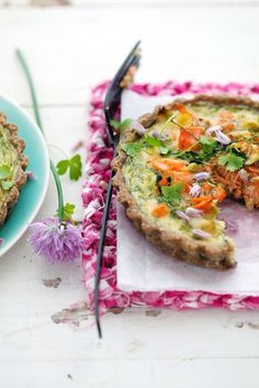 a quiche is on a pink and white plate next to a blue plate with a piece of bread