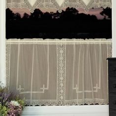 the window is decorated with white lace and has flowers in front of it, along with a black chest of drawers