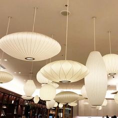 many white lamps hanging from the ceiling in a room with people sitting at tables and chairs