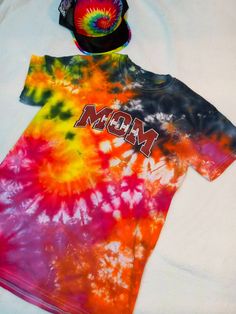 a tie - dyed shirt and hat laying on top of a white sheet with the word mom printed on it