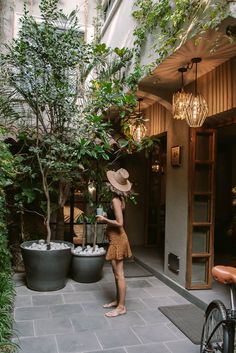 a woman standing in front of a tree with two large potted trees behind her