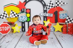 a baby boy sitting on the floor in front of race themed backdrops and signs