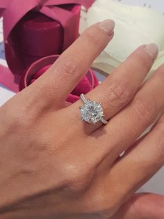 a woman's hand with a diamond ring on it and a pink ribbon in the background