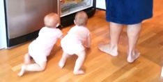 two babys playing with an open refrigerator in the kitchen while their mother watches them