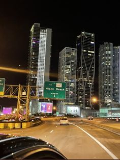 cars driving down the highway at night in front of tall buildings and skyscrapers on either side